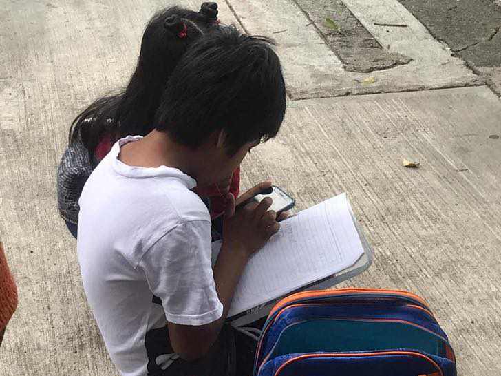 psicologiasdobrasil.com.br - Irmãozinhos assistem às aulas na rua, sentados no chão, usando internet pública