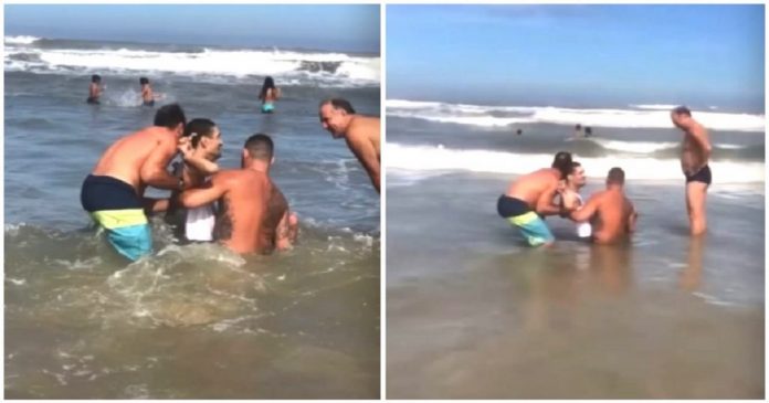 Homens ajudam pai a levar seu filho com deficiência para tomar seu primeiro banho de mar